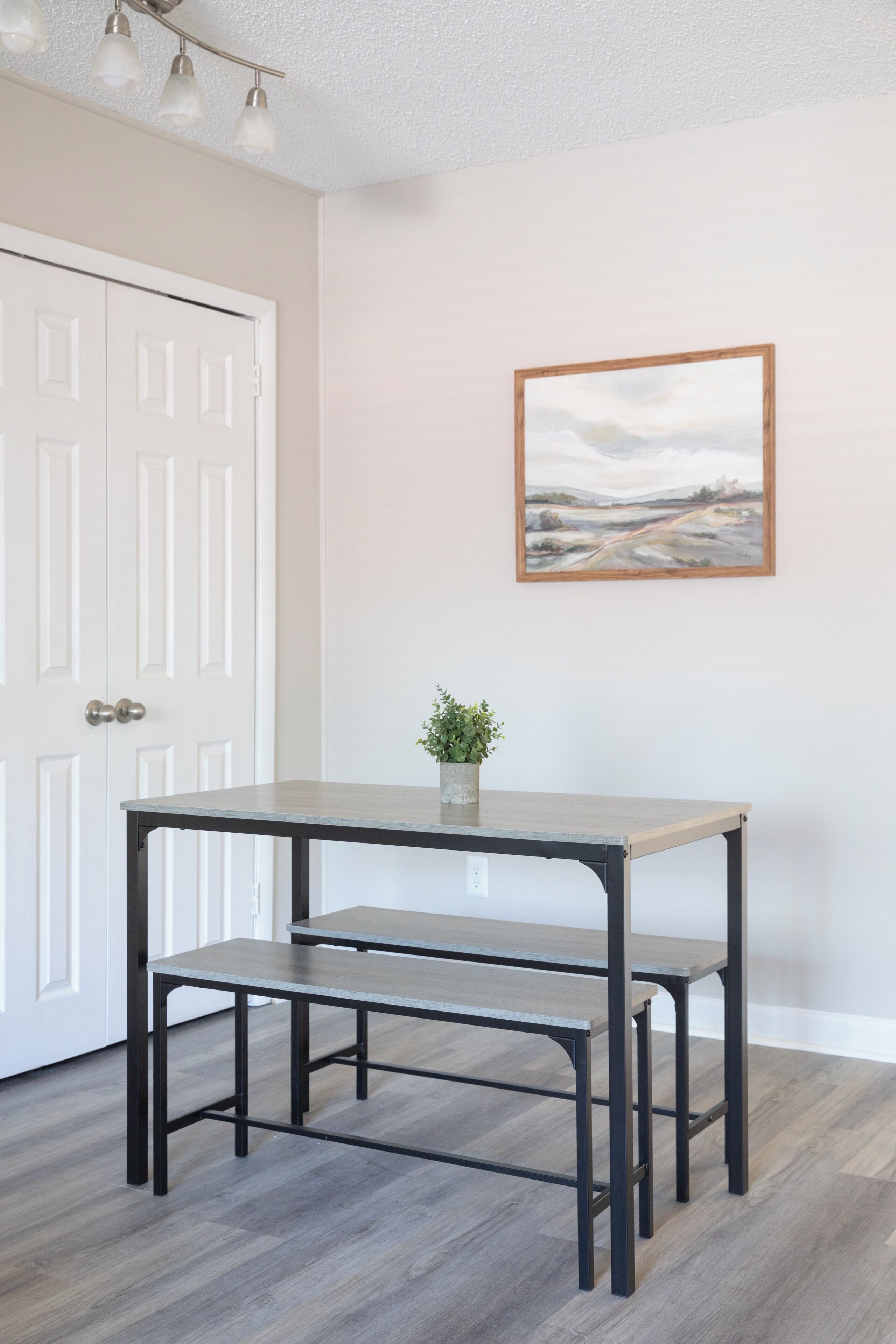 A room with a white door, a painting on the wall, and a table with benches.