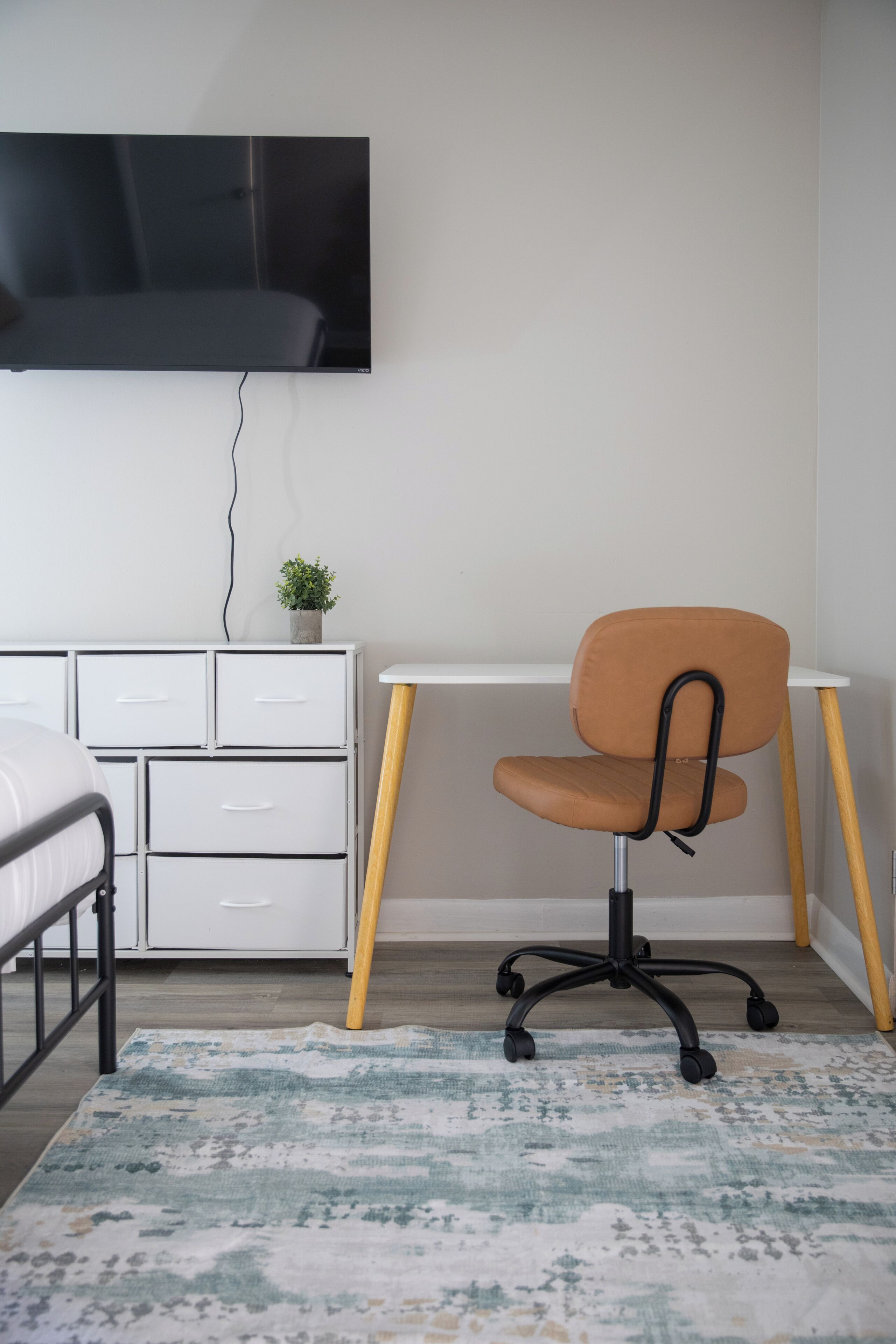 A bedroom with a bed, a desk, a chair, a television, and a small plant.