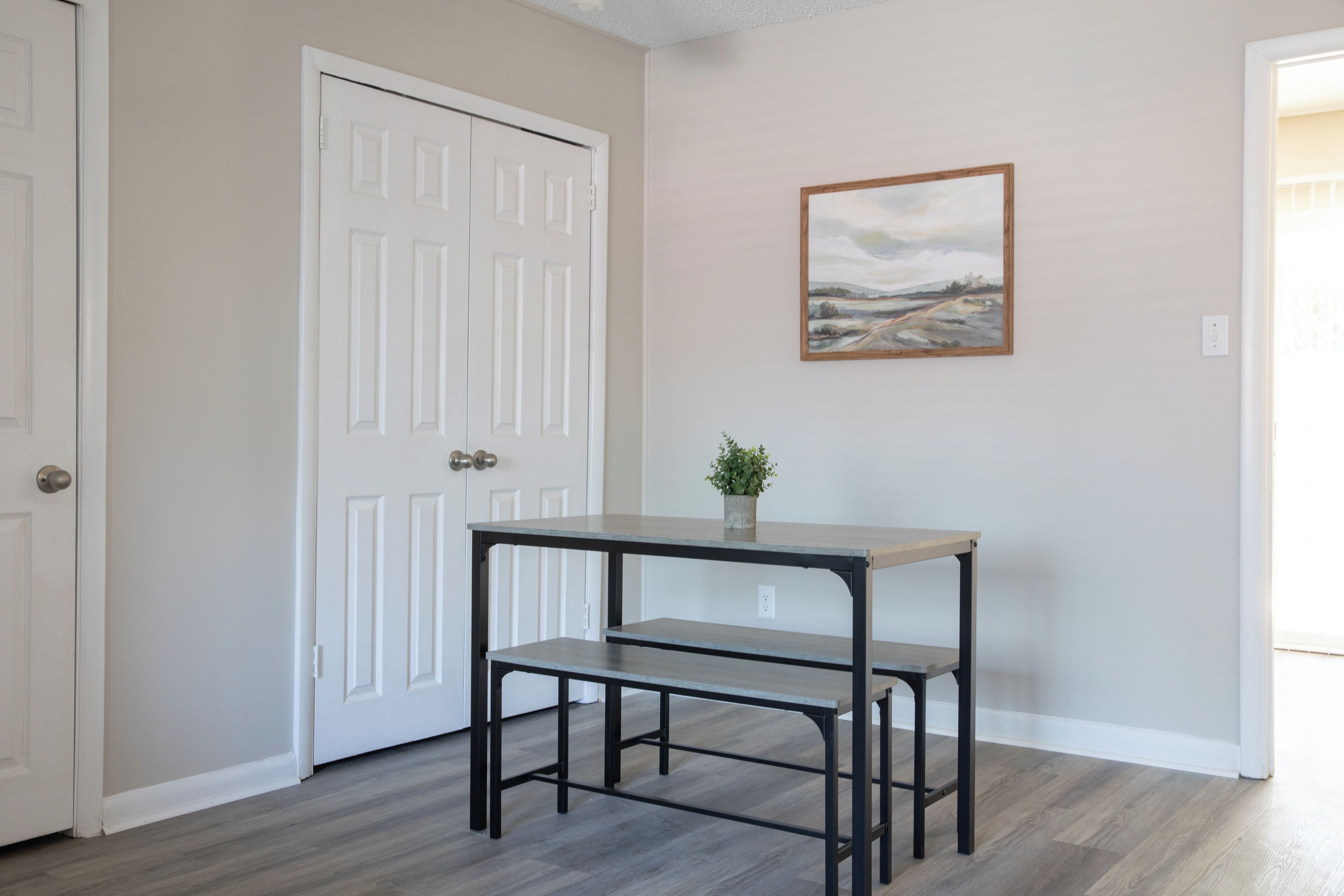 A room with a white door, a painting on the wall, and a small table with a plant.