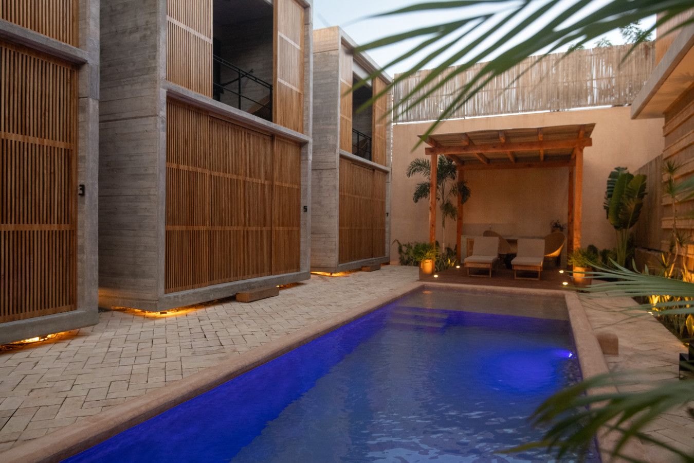 A pool area with a blue pool, wooden fences, and a seating area with chairs and plants.