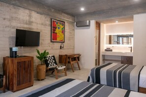 A modern bedroom with a bed, a desk, a chair, a television, and a bathroom visible through an open door. - Jilöo- Beautiful Oasis in Punta Zicatela (7) (Punta Zicatela)
