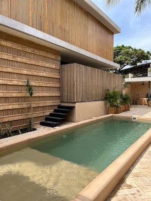 A modern building with a pool, wooden paneling, and a staircase leading to an upper level.