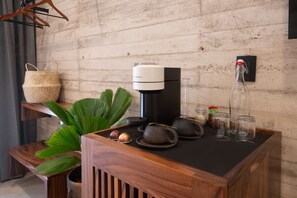 Una mesa de madera con una cafetera, una cesta tejida, una planta en maceta y diferentes vasos.
