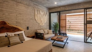 Ein modernes Schlafzimmer mit einem großen Bett, einer Couch und einem Couchtisch. Eine Glastür führt zu einem Balkon mit Blick auf eine Bambus-Umzäunung.