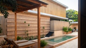 Ein moderner Poolbereich im Freien mit einer Holzterrasse, Liegestühlen und einer Treppe zu einer überdachten Terrasse.