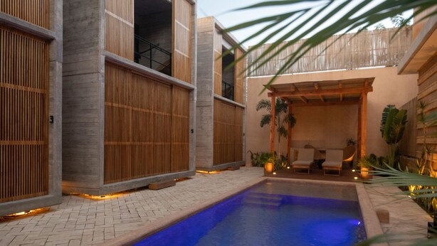 Un espace piscine avec une piscine bleue, des clôtures en bois et un coin salon comprenant des chaises et des plantes.