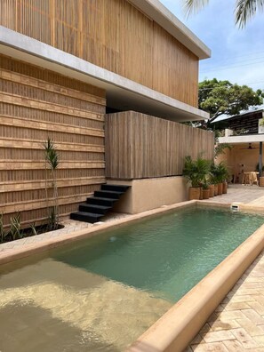 A modern building with a pool, wooden paneling, and a staircase leading to an upper level.