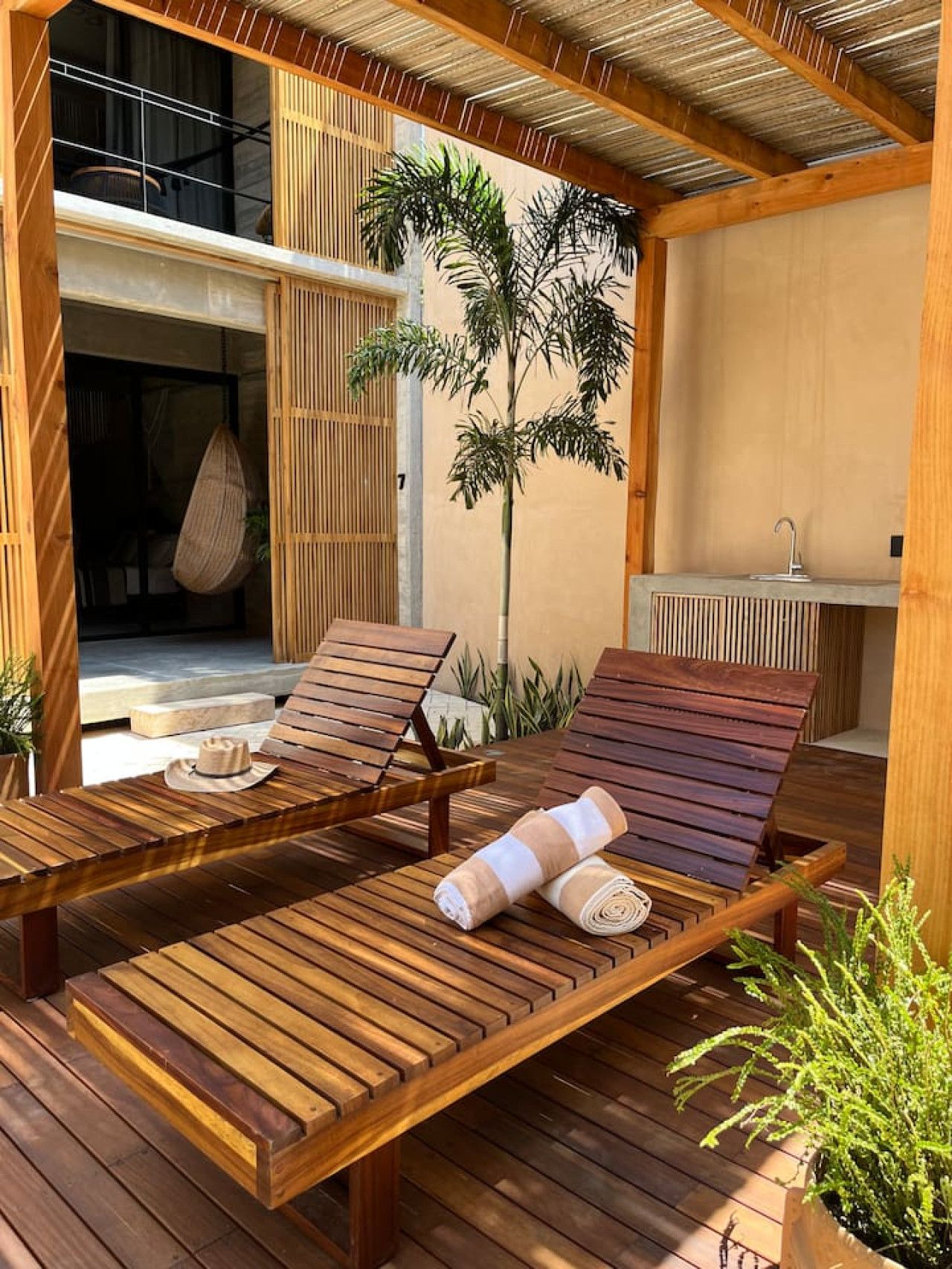 Une terrasse en bois avec deux chaises longues, un fauteuil suspendu et une petite table.