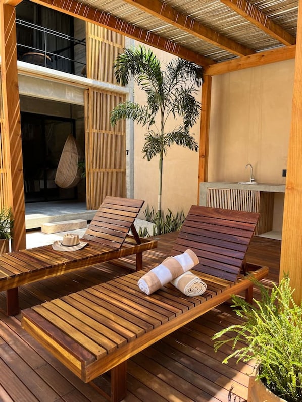 A wooden deck with two lounge chairs, a hanging chair, and a small table.