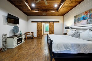 Ein Schlafzimmer mit einem Bett, einem an der Wand montierten Fernseher, einem Kamin und einem großen Fenster.