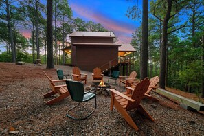 Eine Holzhütte mit einer Terrasse, umgeben von Bäumen, mit Holzstühlen und einem Feuerkorb.