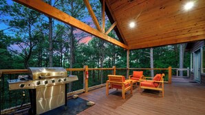 An outdoor deck with a grill, wooden chairs, and a view of trees. - Secluded Cabin | Hot Tub | Game Loft (Broken Bow)