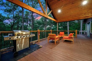Eine Terrasse im Freien mit Grill, Holzstühlen und Blick auf Bäume.