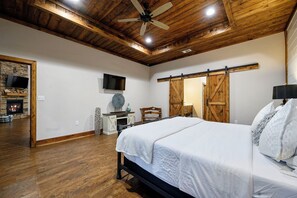 A bedroom with a large bed, a ceiling fan, a fireplace, and a TV mounted on the wall. - Secluded Cabin | Hot Tub | Game Loft (Broken Bow)