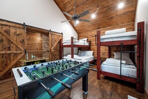 A room with wooden walls, a ceiling fan, bunk beds, and a foosball table. - Secluded Cabin | Hot Tub | Game Loft (Broken Bow)