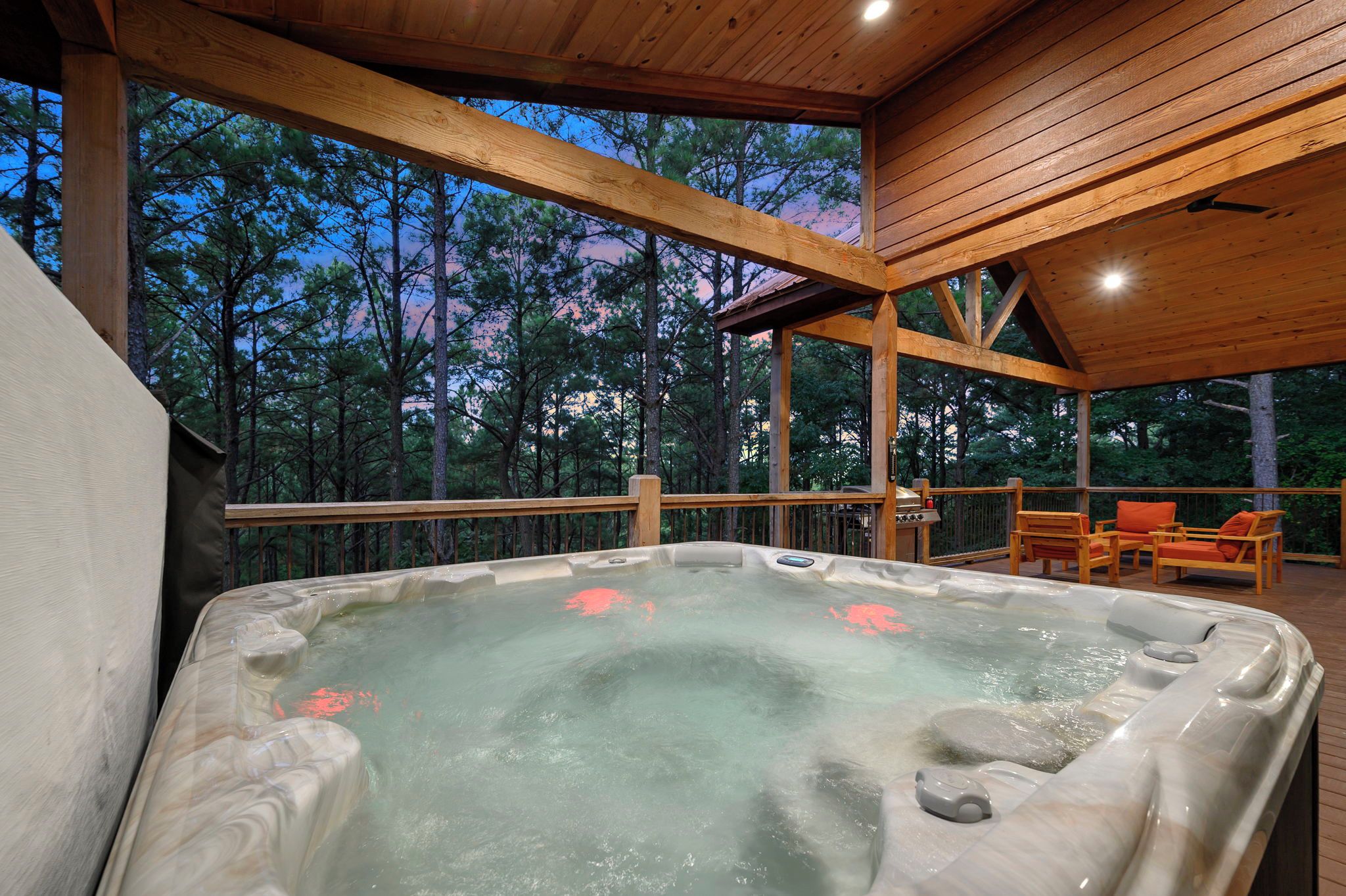 Een hottub in een overdekte buitenruimte met houten balken en uitzicht op bomen.