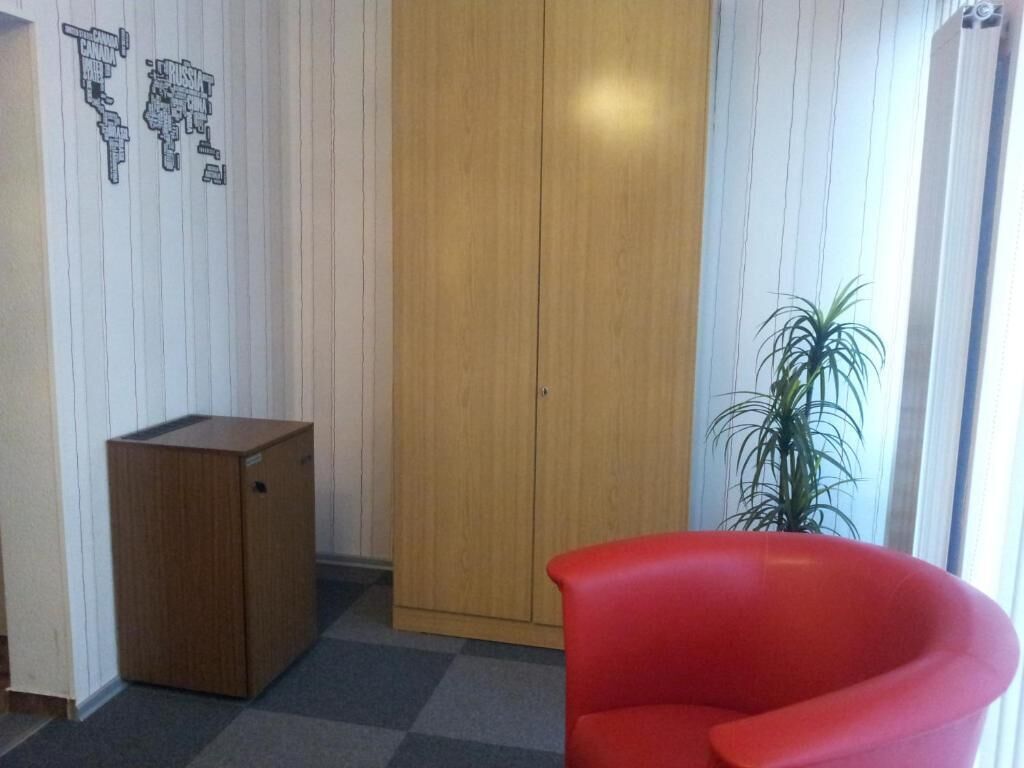 A room with a wooden wardrobe, a red chair, and a potted plant.
