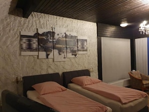 A bedroom with two beds, a large wall art piece, a chair, and a sliding door.