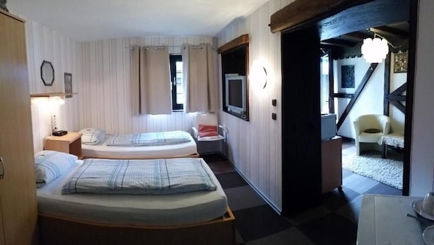 A room with two beds, a desk, a chair, and a television. There is a door leading to another room. - Hotel am Hallenbad (Ratingen)