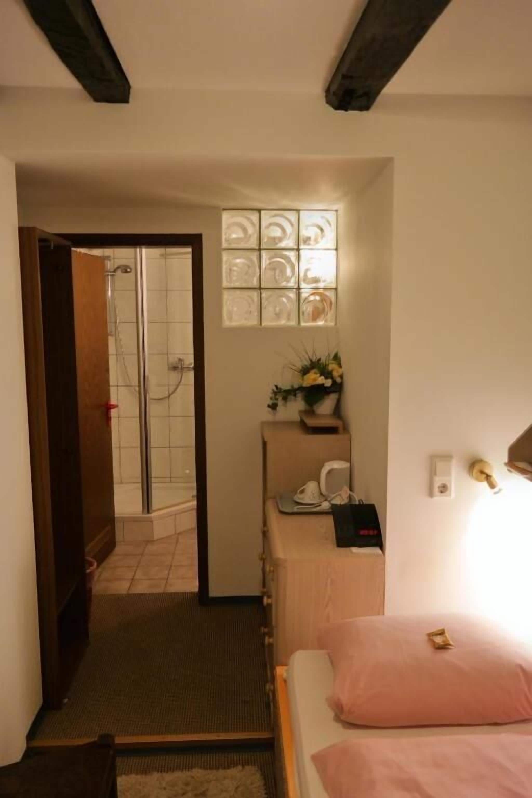 Ein Hotelzimmer mit Bett, Schreibtisch, Stuhl, einem kleinen Tisch mit Vase sowie einer Dusche.