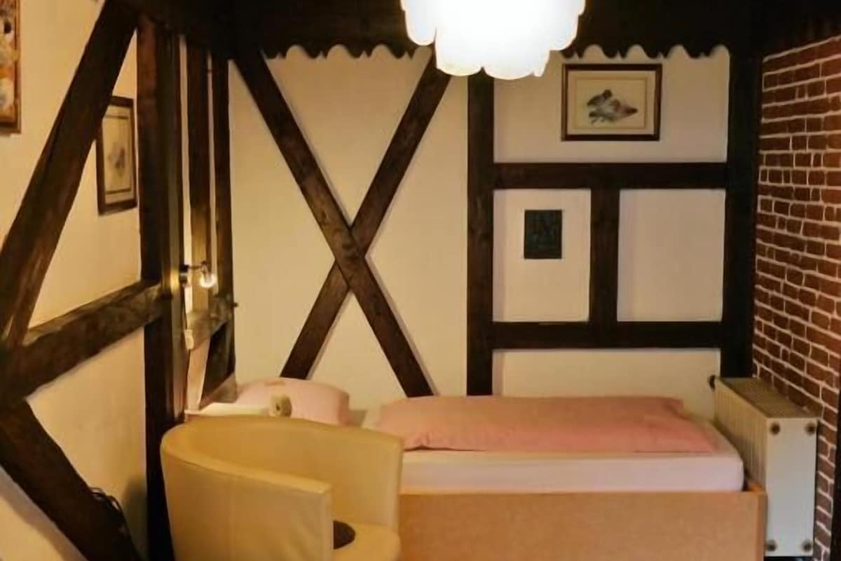 A cozy room with a bed, a chair, a small table, and a hanging light fixture.