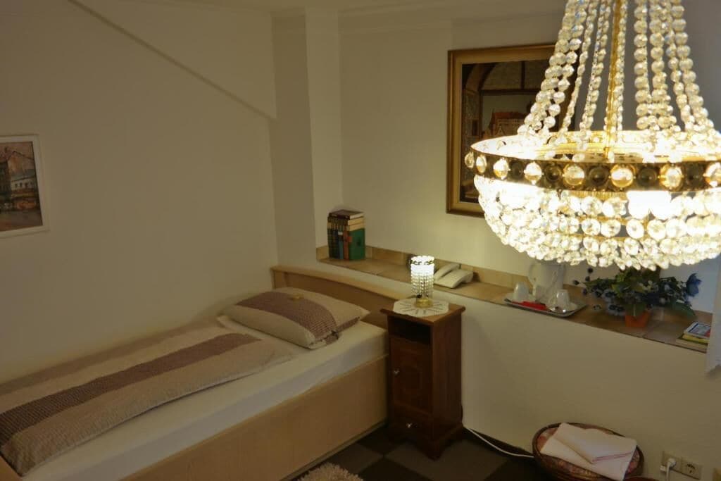 A bedroom with a bed, bedside table, lamp, and a chandelier.