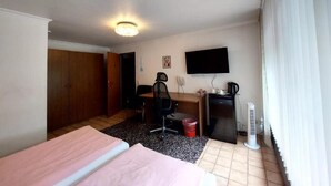 A hotel room with a bed, desk, chair, television, and a heater. - Hotel am Hallenbad (Ratingen)