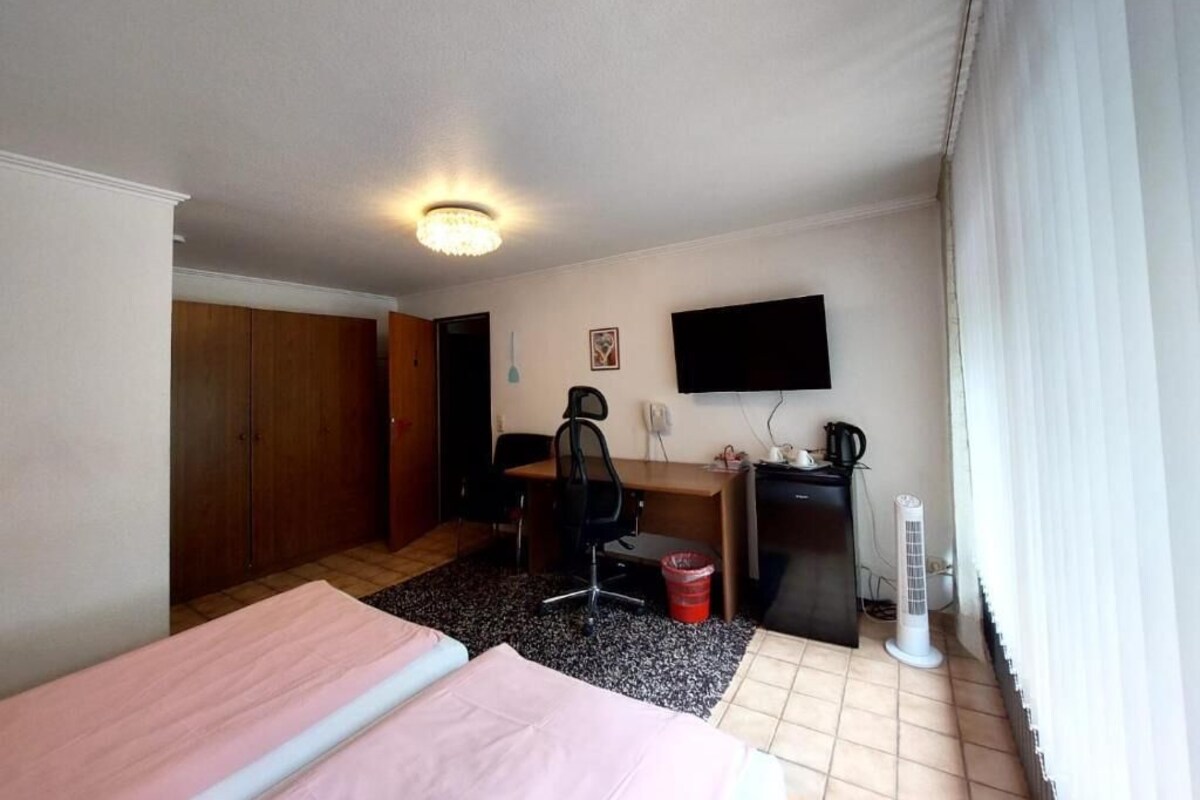 A hotel room with a bed, desk, chair, television, and a heater.
