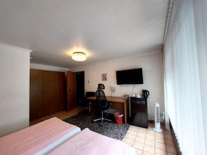A hotel room with a bed, desk, chair, television, and a heater. - Hotel am Hallenbad (Ratingen)