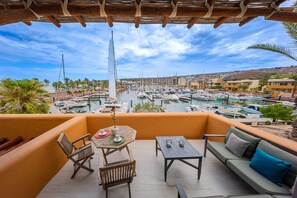 A balcony with a view of a marina, wooden furniture, and a clear sky. - Puerta Cortés 404 - 2BD Marina View Condo (La Paz)