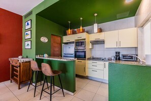 Une cuisine avec un mur d’accent vert, un comptoir-bar en bois, deux tabourets de bar, un four à micro-ondes, un four traditionnel et une machine à café.