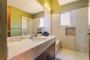 A bathroom with a sink, mirror, and shower. - Puerta Cortés 404 - 2BD Marina View Condo (La Paz)