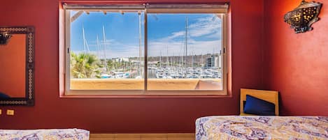 Habitación con dos camas, un ventanal con vista a un puerto deportivo y una lámpara fijada a la pared.