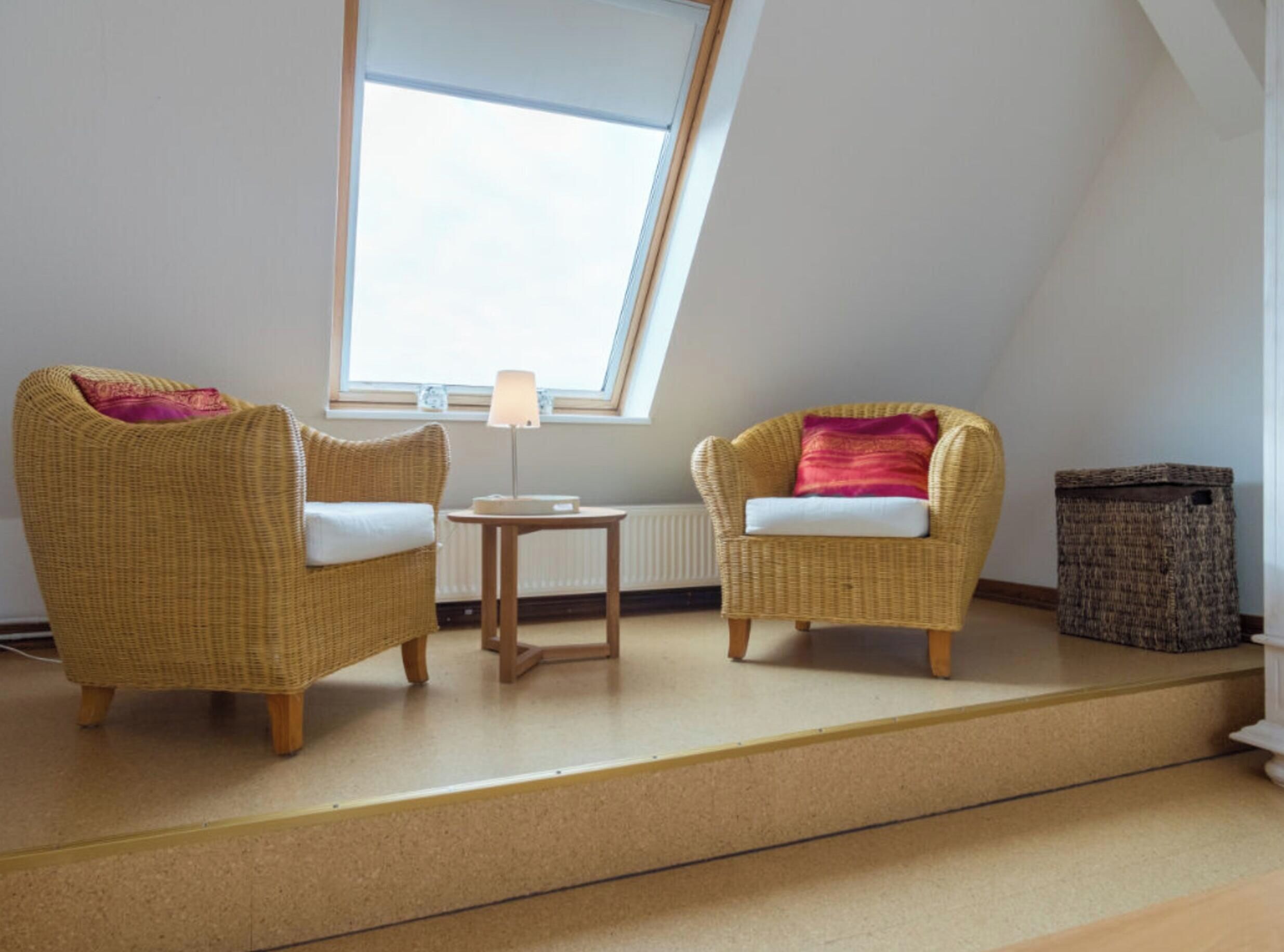 A room with two wicker chairs, a small table, a lamp, a radiator, and a trash bin.