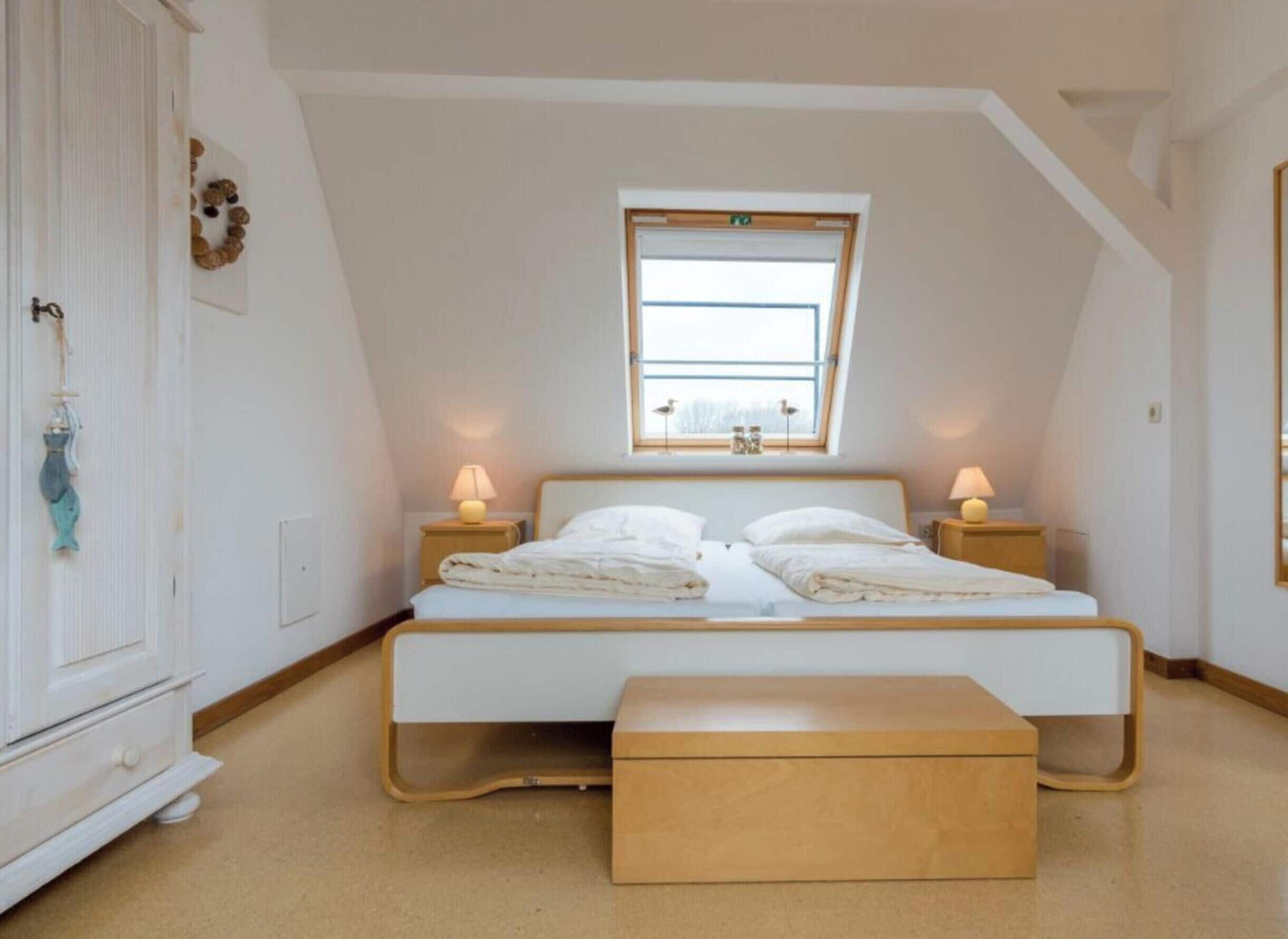 A bedroom with a bed, bedside lamps, a window, and a wooden bench.