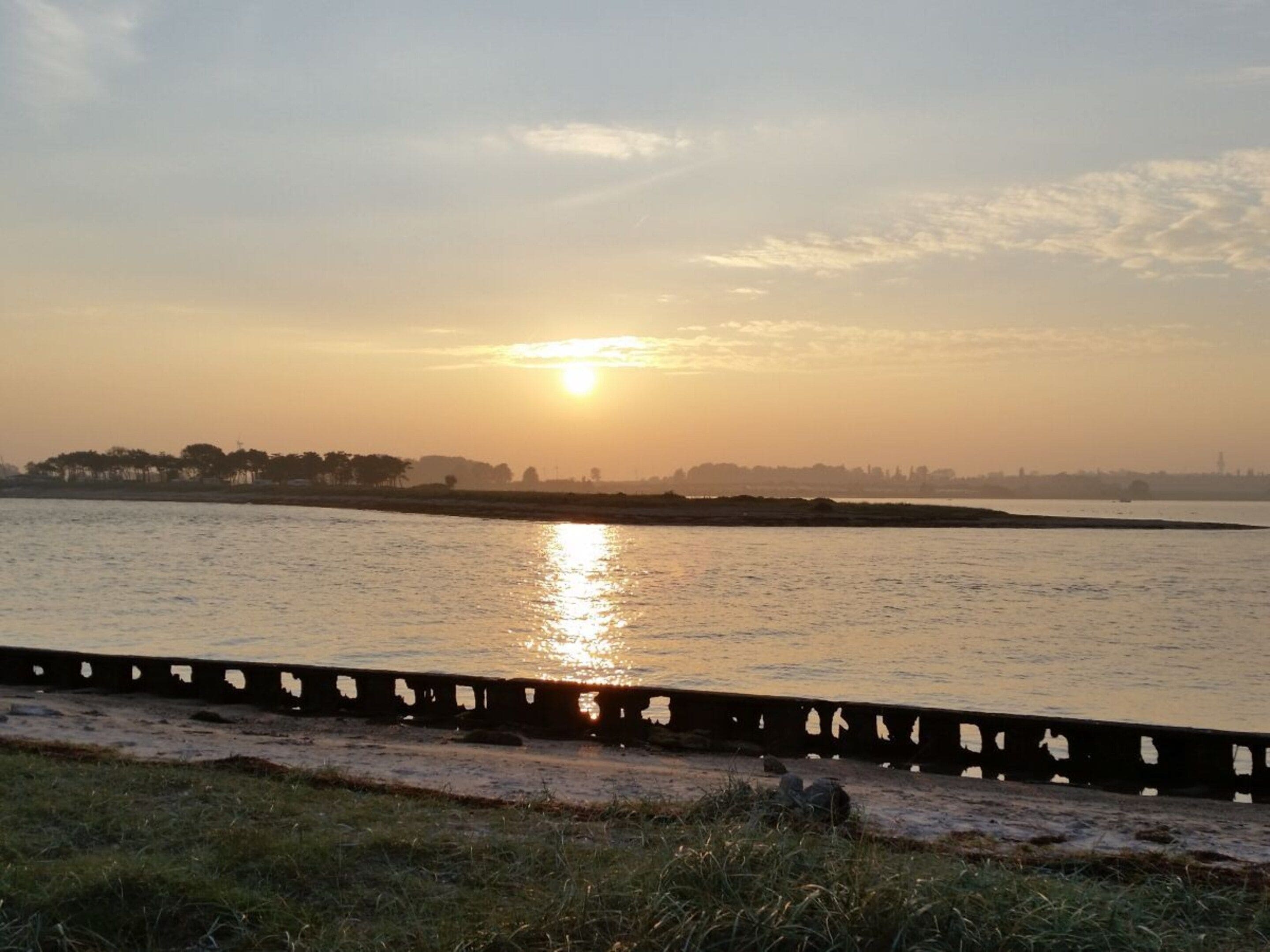 A sunset over a calm body of water with a distant city skyline.