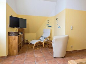 Une pièce comprenant une télévision, une étagère en bois, un fauteuil à bascule, un fauteuil blanc et un mur décoré d’autocollants représentant des poissons.