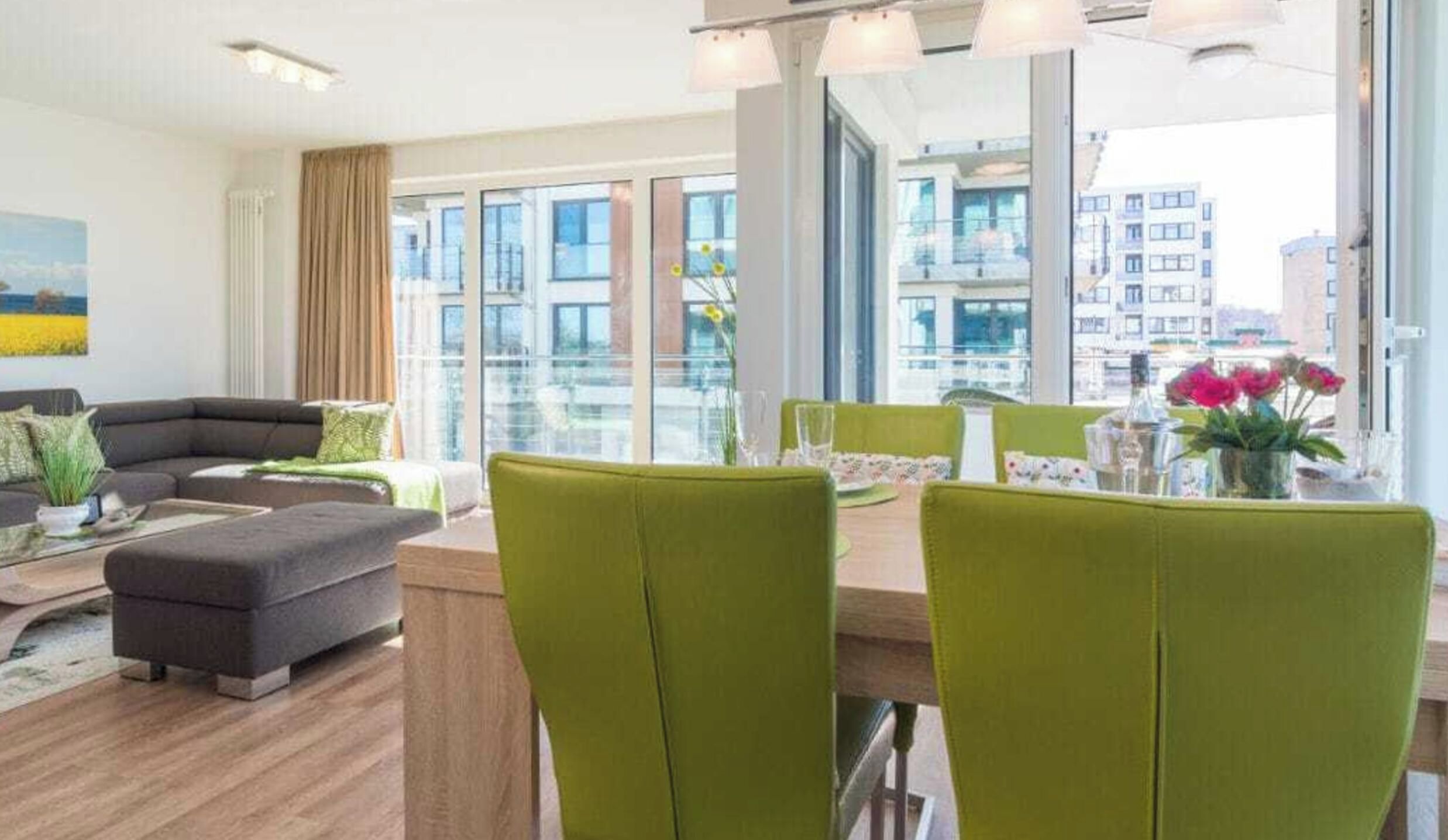 A modern living room with a sofa, ottoman, and dining table with chairs. Large windows offer a view of the cityscape.