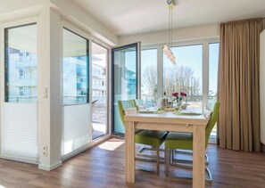 Un'area pranzo moderna con un tavolo in legno, sedie verdi e vista sugli edifici attraverso ampie finestre.