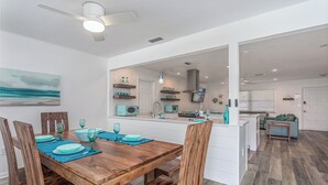 A modern kitchen with a central island, wooden dining table with chairs, and a view into the living area. - Island Time (Sarasota)