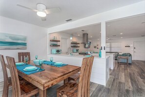 A modern kitchen with a central island, wooden dining table with chairs, and a view into the living area. - Island Time (Sarasota)