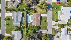 An aerial view of a residential area with houses, a swimming pool, and a red car parked on the street. - Island Time (Sarasota)