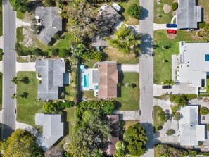 An aerial view of a residential area with houses, a swimming pool, and a red car parked on the street. - Island Time (Sarasota)