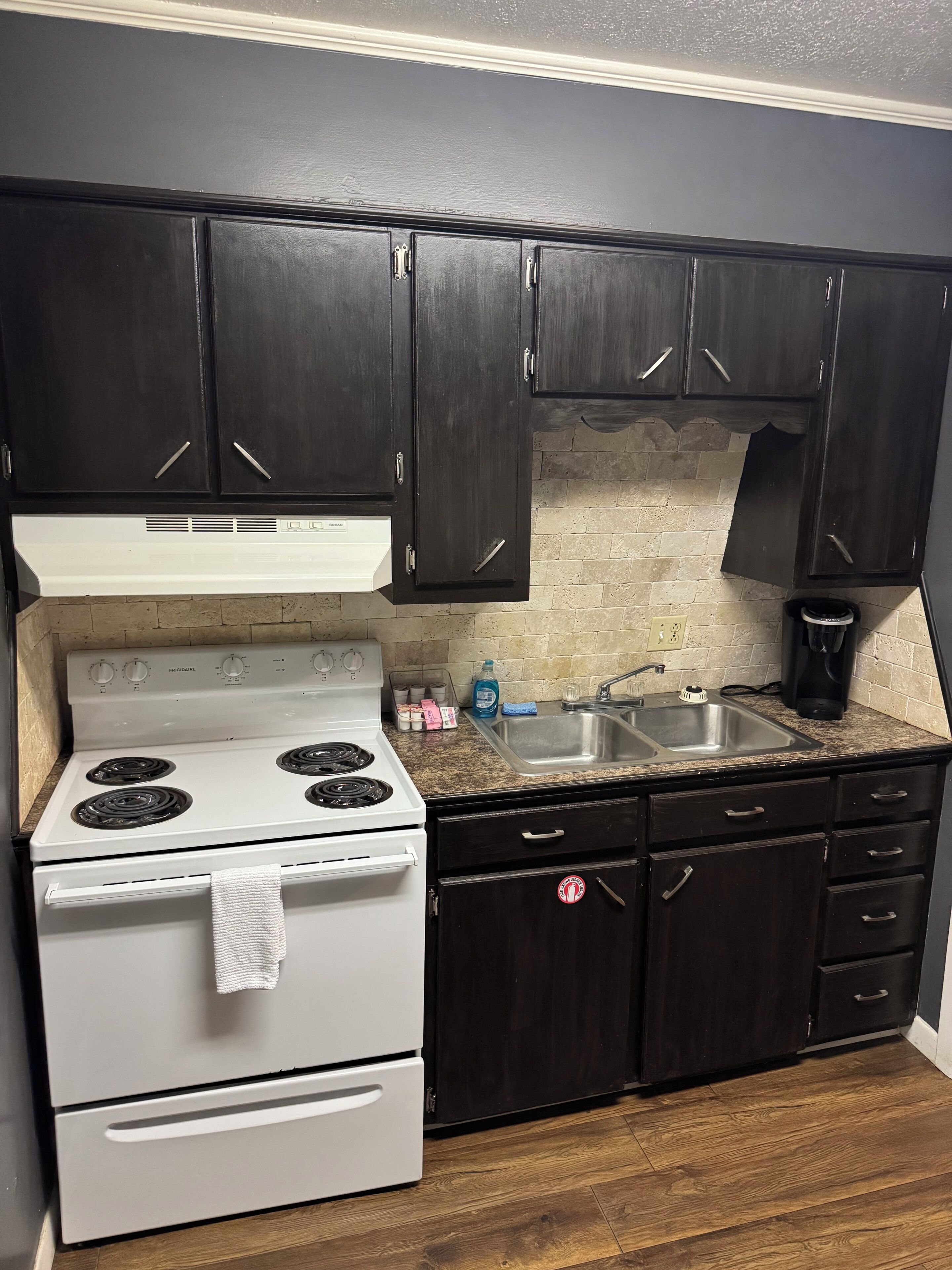 A kitchen with dark cabinets, a white stove, a sink, and a countertop with various items.