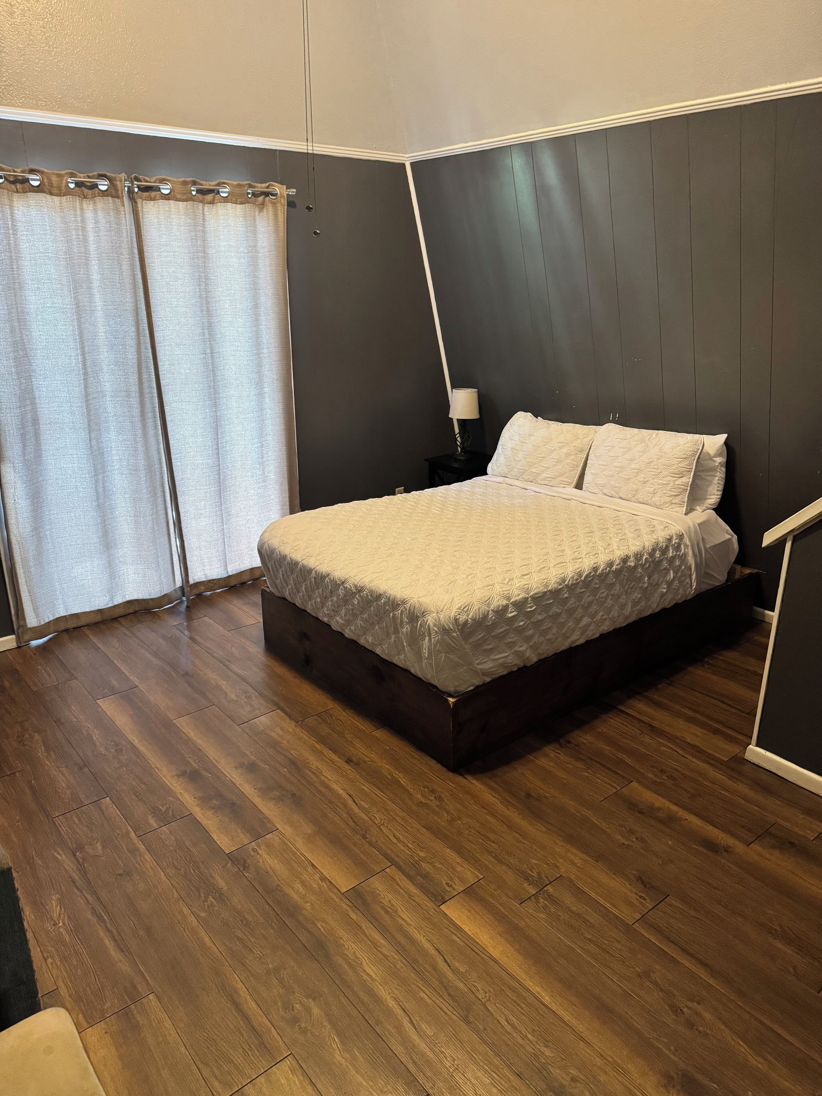A bedroom with a bed, a nightstand, a lamp, and a window with curtains.