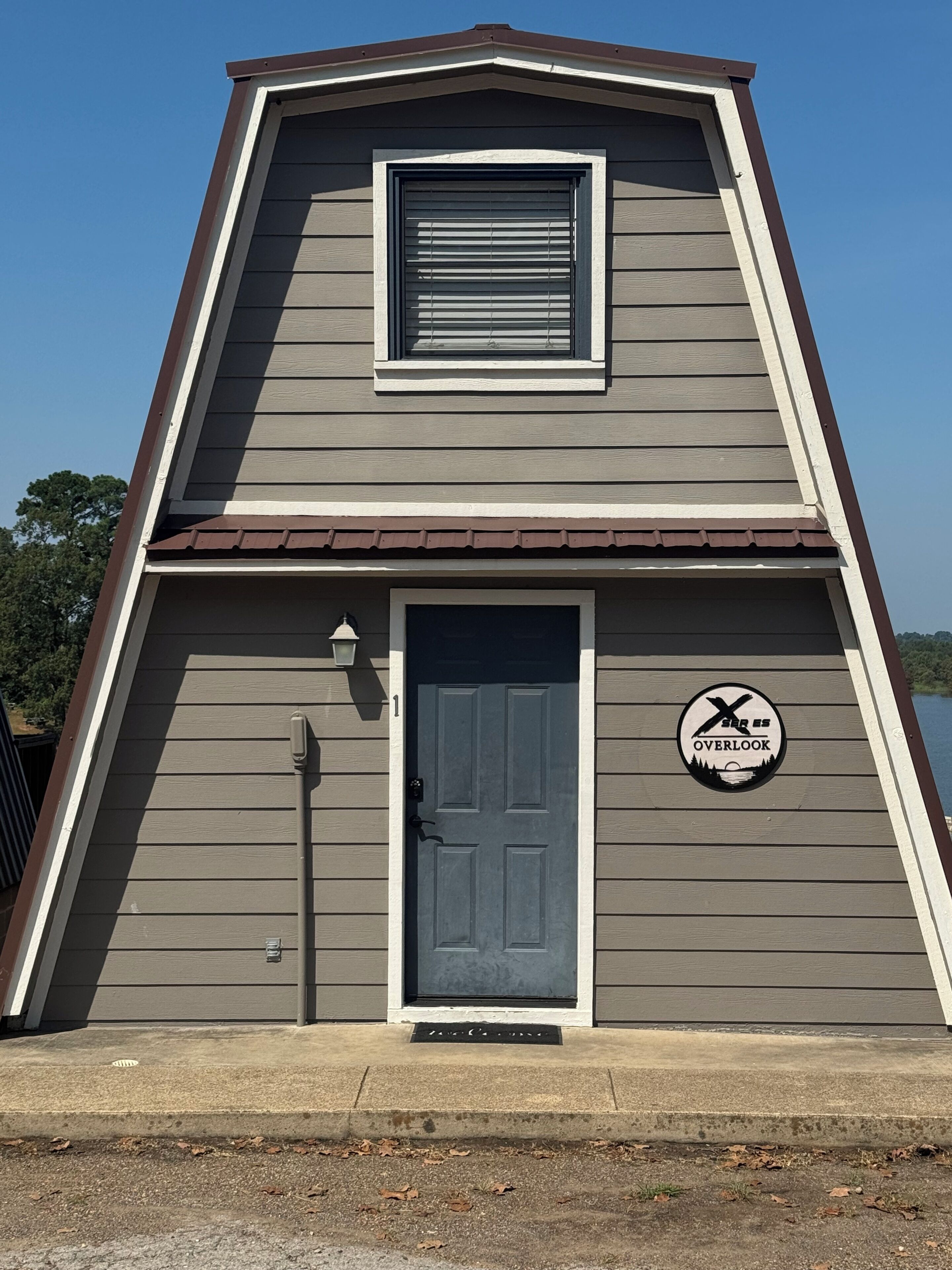 A two-story building with a dark gray siding exterior, a brown roof, and a single door with a window above it.