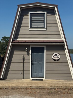 A two-story building with a dark gray siding exterior, a brown roof, and a single door with a window above it.