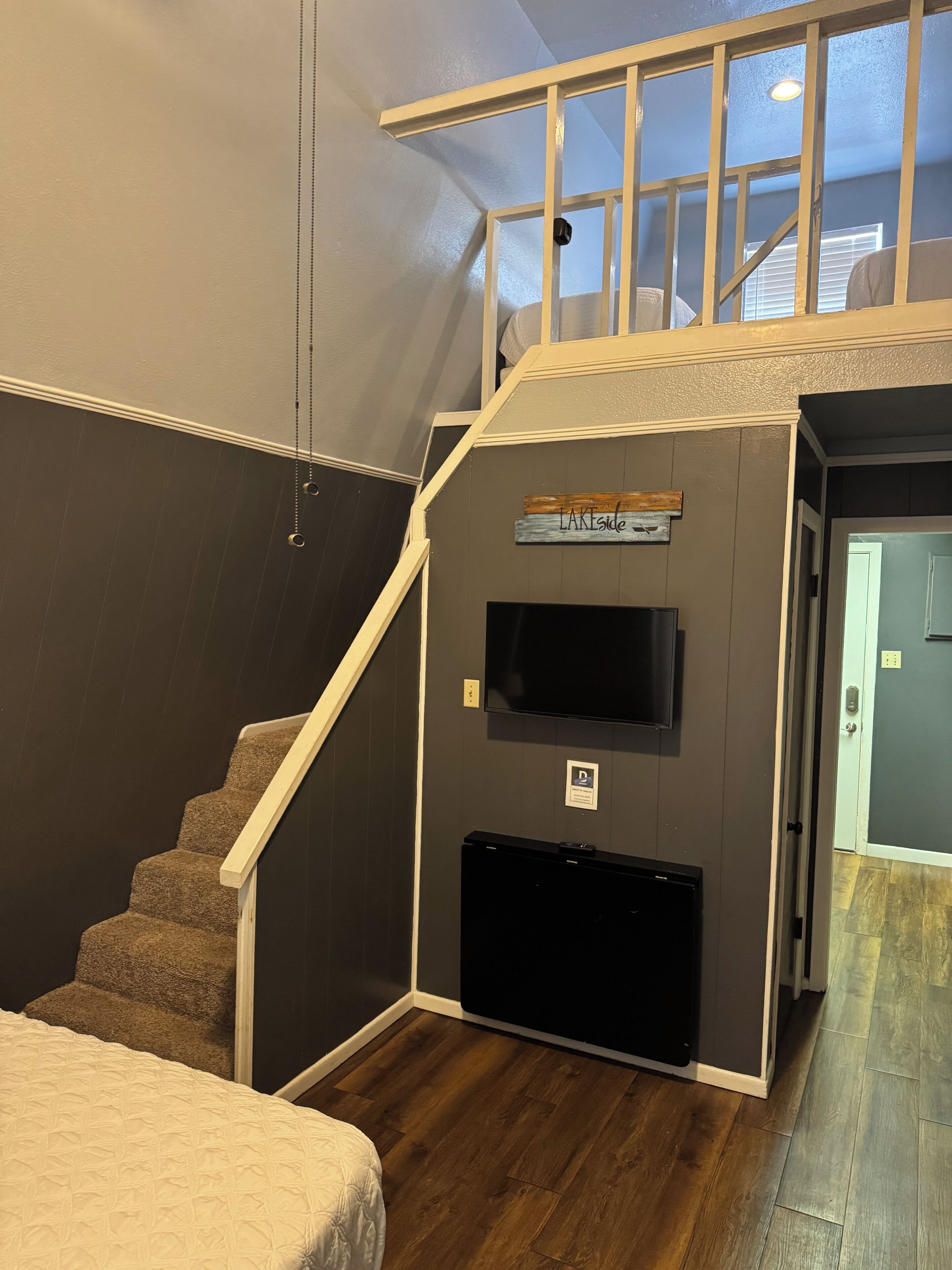A staircase with a handrail, a flat-screen TV mounted on the wall, and a sign that reads 'LAKside.'
