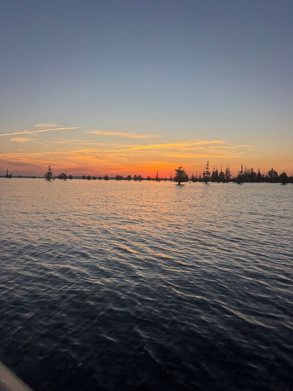 A calm body of water with a distant shoreline, trees, and a clear sky.