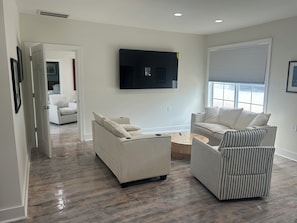 A modern living room with a flat-screen TV mounted on the wall, a sofa, a striped armchair, and a coffee table. - Newly rennovated Two bedroom waterfront Get Away. (Morehead City)